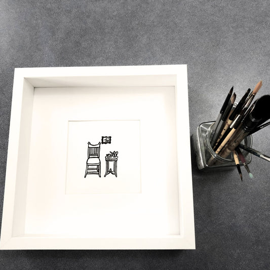 Lino print, hand printed by Helen Gray. Cozy Corner.  A chair and table with teapot and cup, and a cat picture on the wall.