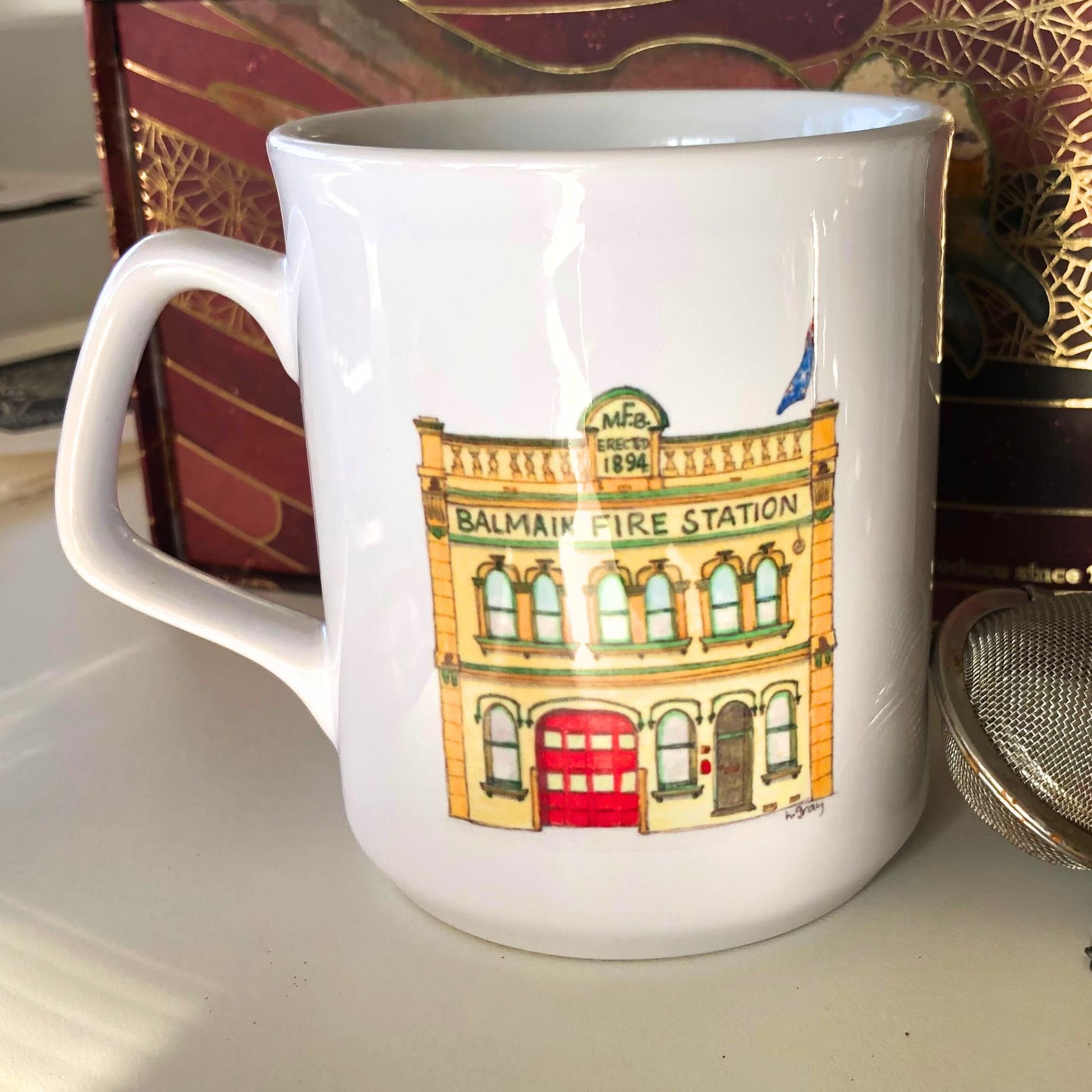 White coffee mug showing a watercoloured, yellow and red painting of the old Balmain Fire Station in Sydney, a building from the Victorian era. From original artwork.