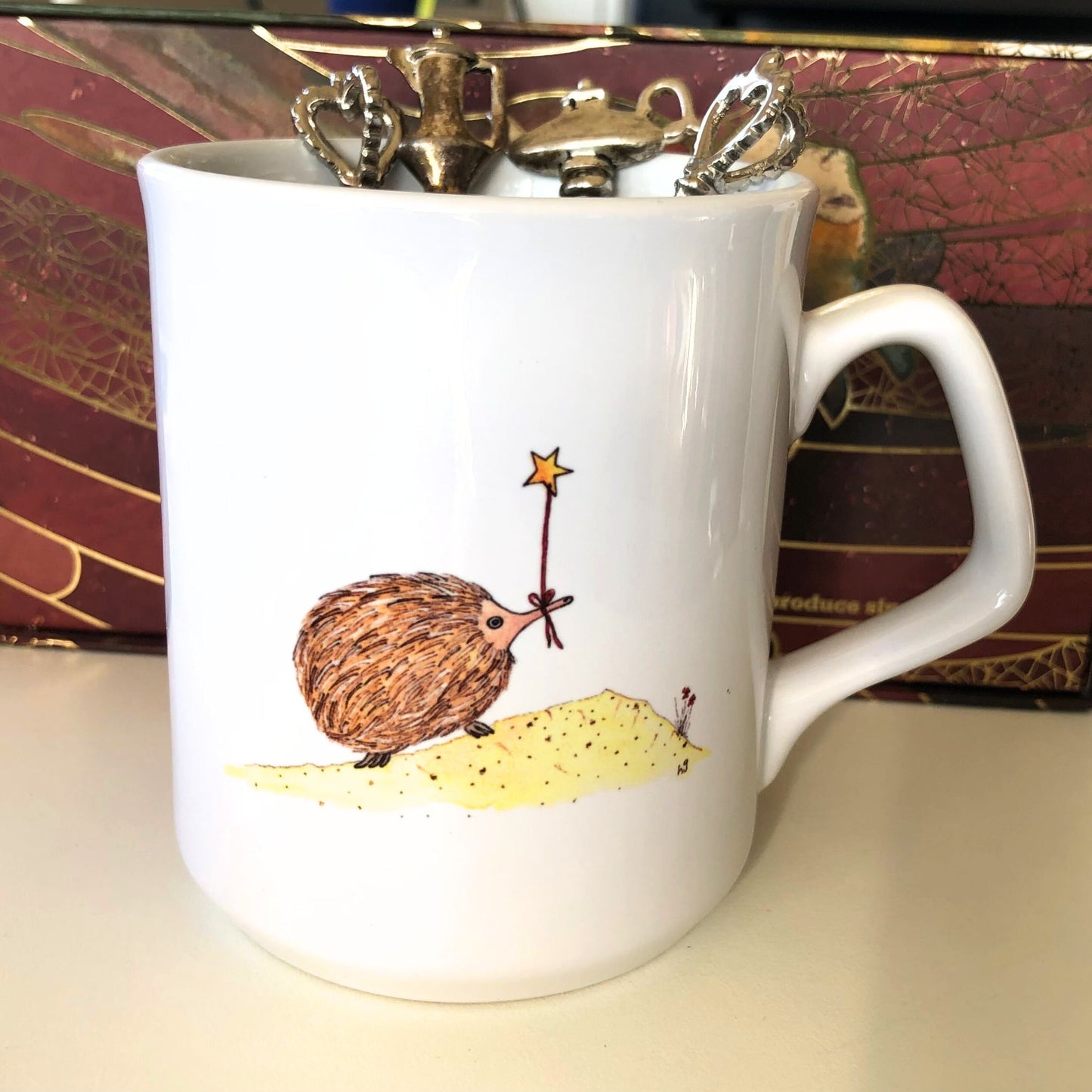 White coffee mug featuring an Australian echidna holding a gold star on a string. From original artwork.