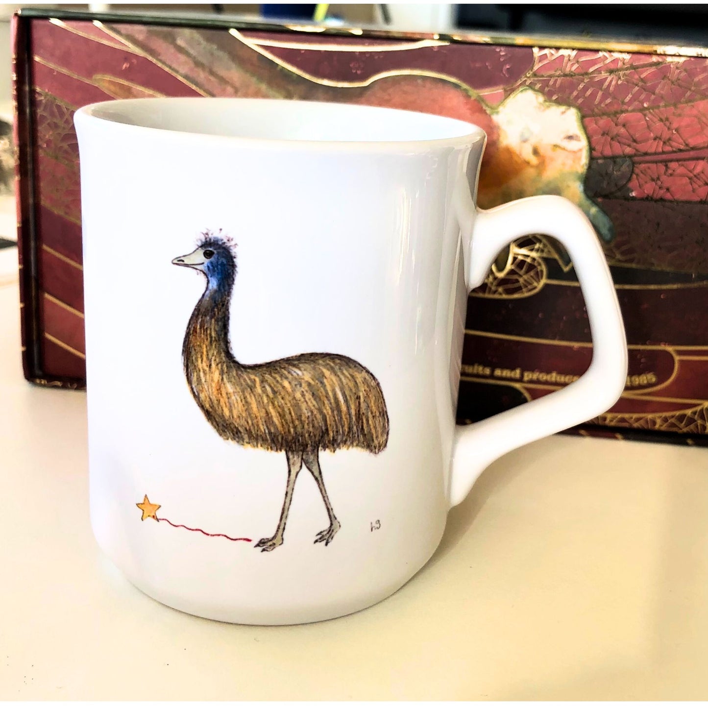 White coffee mug with an emu, holding a gold star on a string. From original artwork.