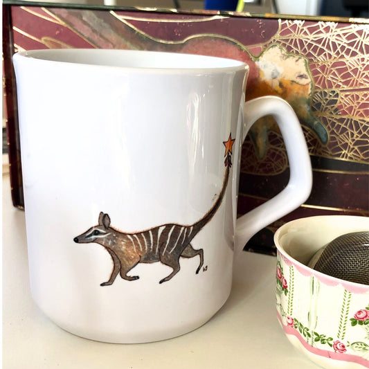 White coffee mug with a brown, striped numbat, holding a gold star on a string. From original artwork.