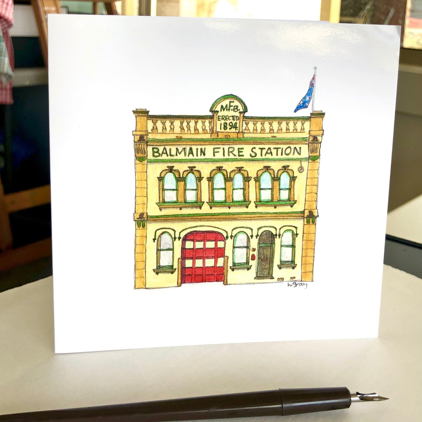 1894 Balmain Fire Station building, painted yellow with green trim and a red door. Australian flag on top of building.