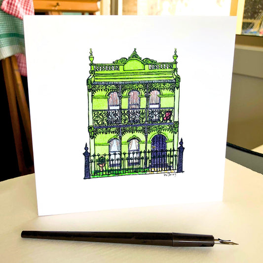 Green Australian terrace house, with decorative filigree and trim on the verandah, and a dark grey door and fence. 