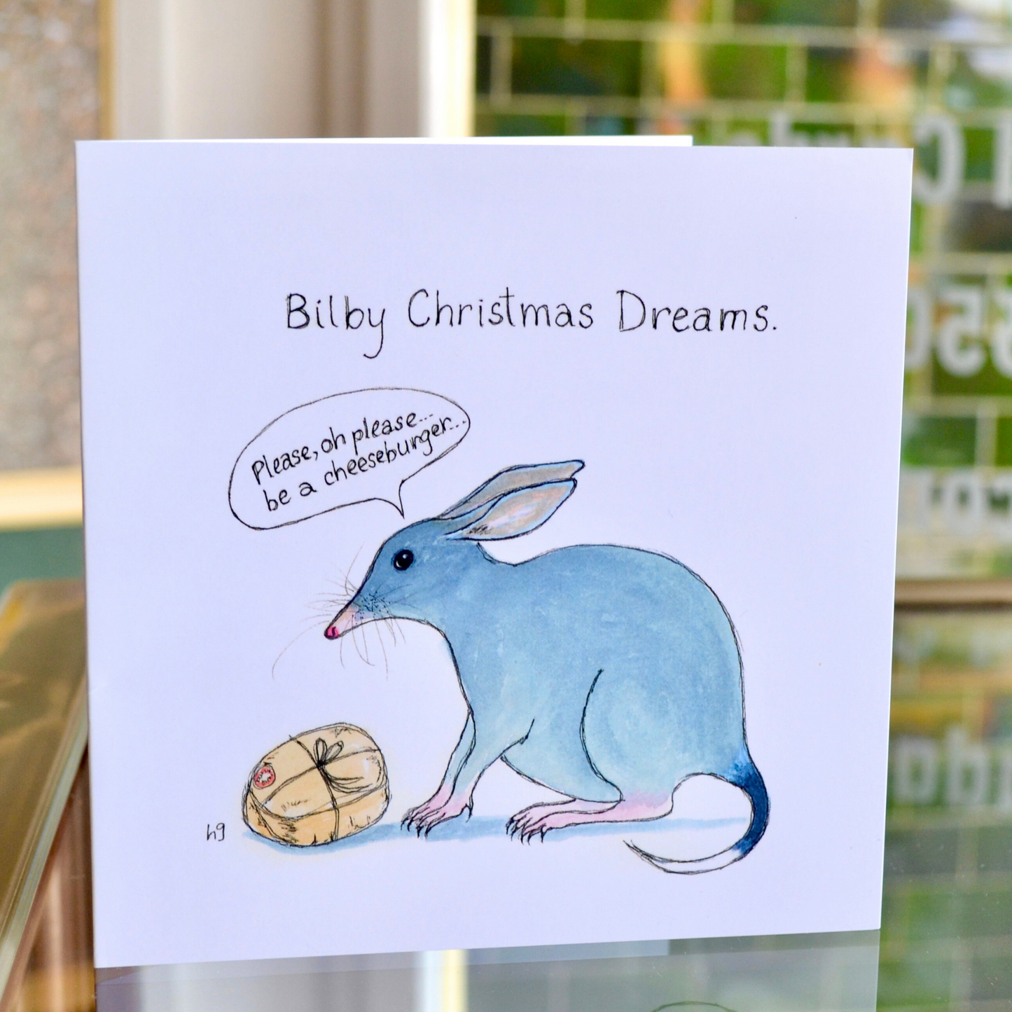 A bilby with a small wrapped parcel and the words "Please, oh please be a cheeseburger'.