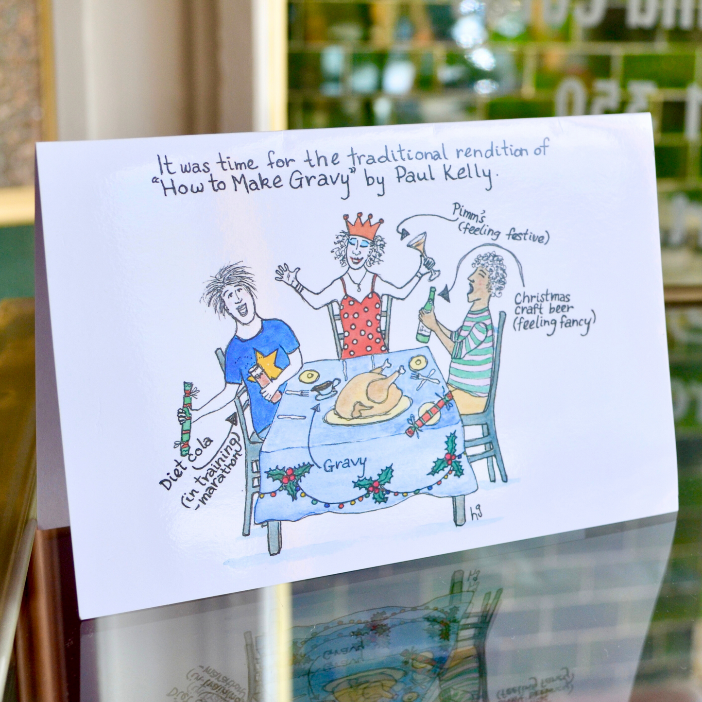 Three people celebrating a Christmas meal, with a turkey, crackers and drinks. It reads "It was time for the traditional rendition of 'How to Make Gravy' by Paul Kelly".