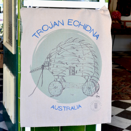 Beige, 100% soft cotton Tea towel, with a humorous drawing of a Trojan echidna in black ink on a light green circular background, and the words "Trojan Echidna Australia" above and below the echidna in a blue font. Comes with a decorative cardboard band.