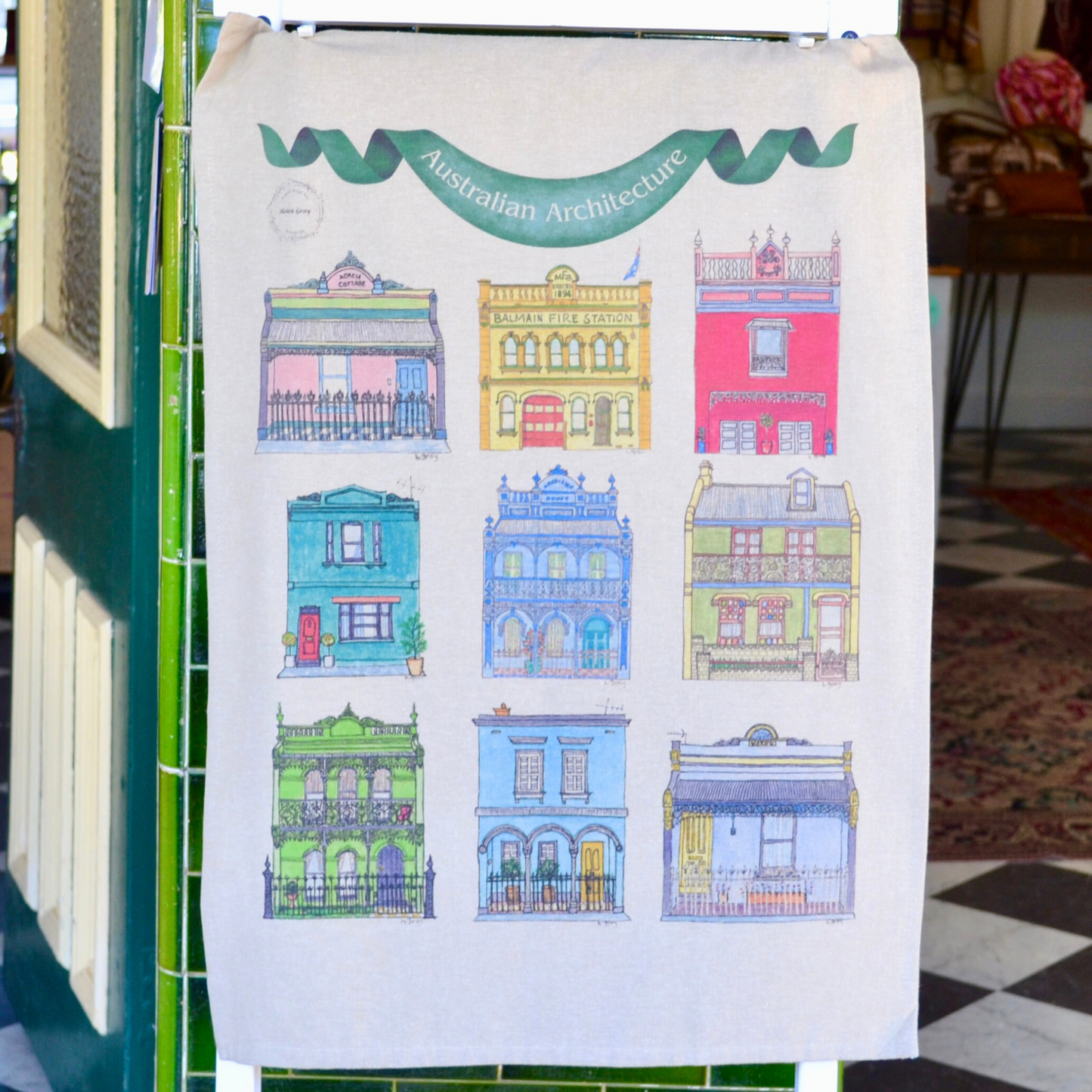 A tea towel with 9  beautiful, colourful Australian buildings from an original watercolour by Helen Gray. Printed on a beige background on 100%soft cotton, with a green banner that says Australian Architecture.